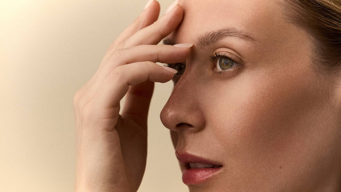 Person touching their forehead and eye area in a close-up skincare portrait.