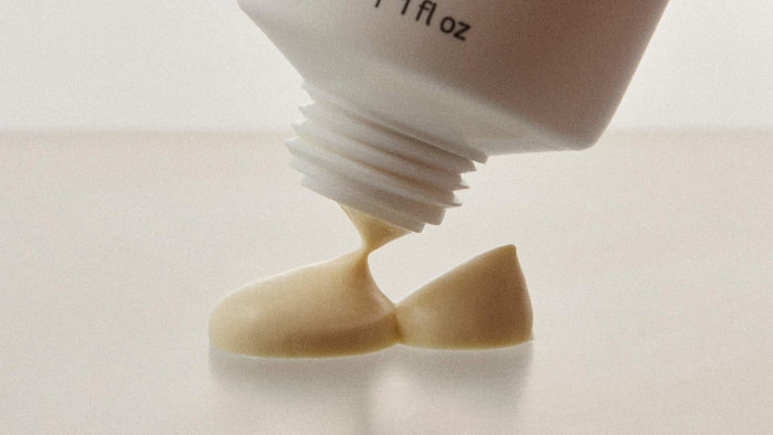 Macro view of a creamy skincare product being squeezed from a tube onto a smooth surface.