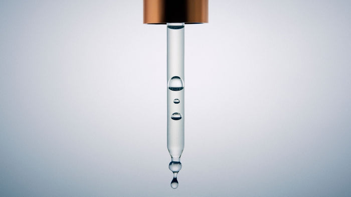 Macro view of a glass dropper filled with clear facial serum, highlighting its lightweight liquid texture.