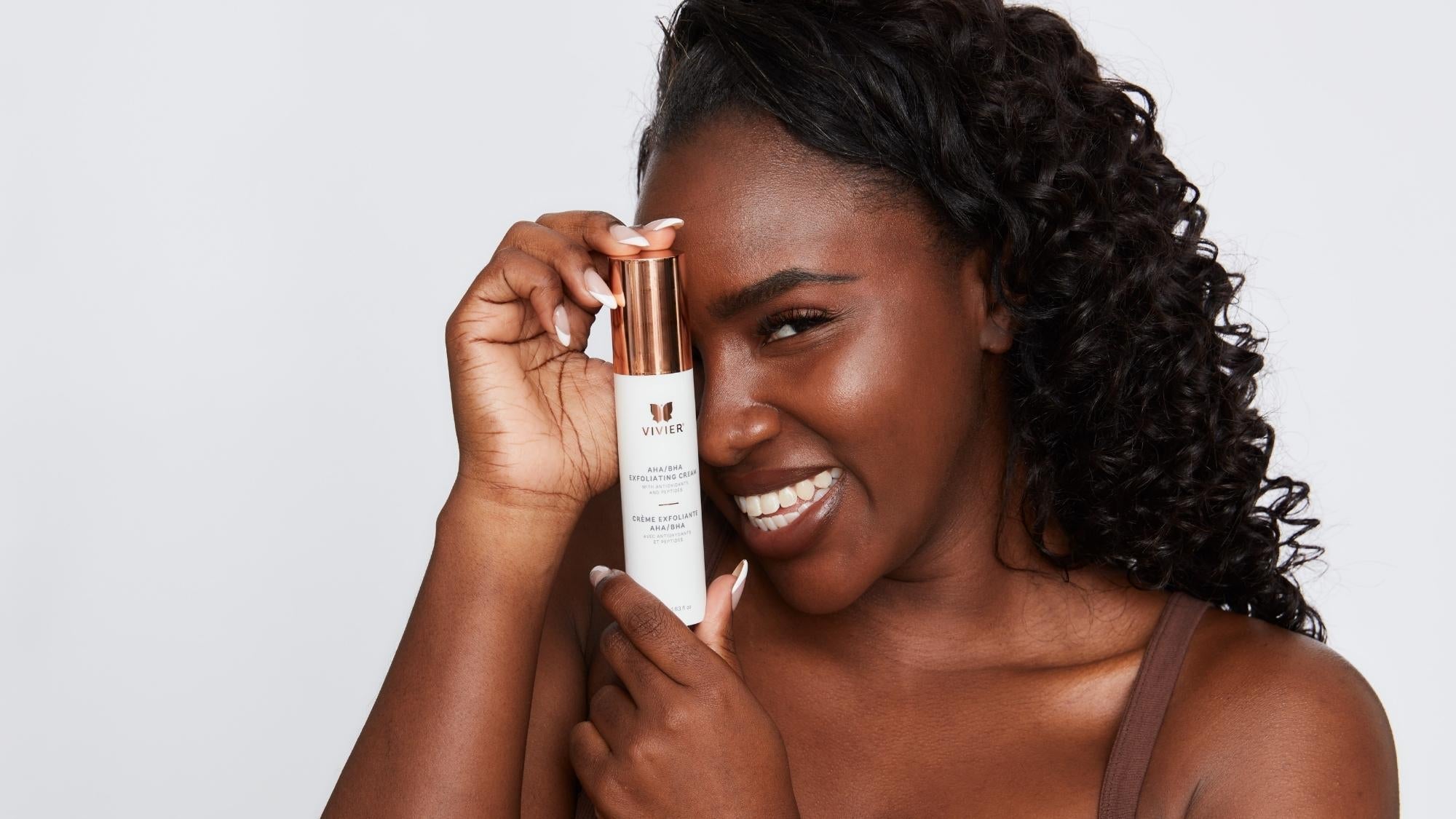 Person holding and smiling with a tube of Vivier AHA BHA Exfoliating Cream.
